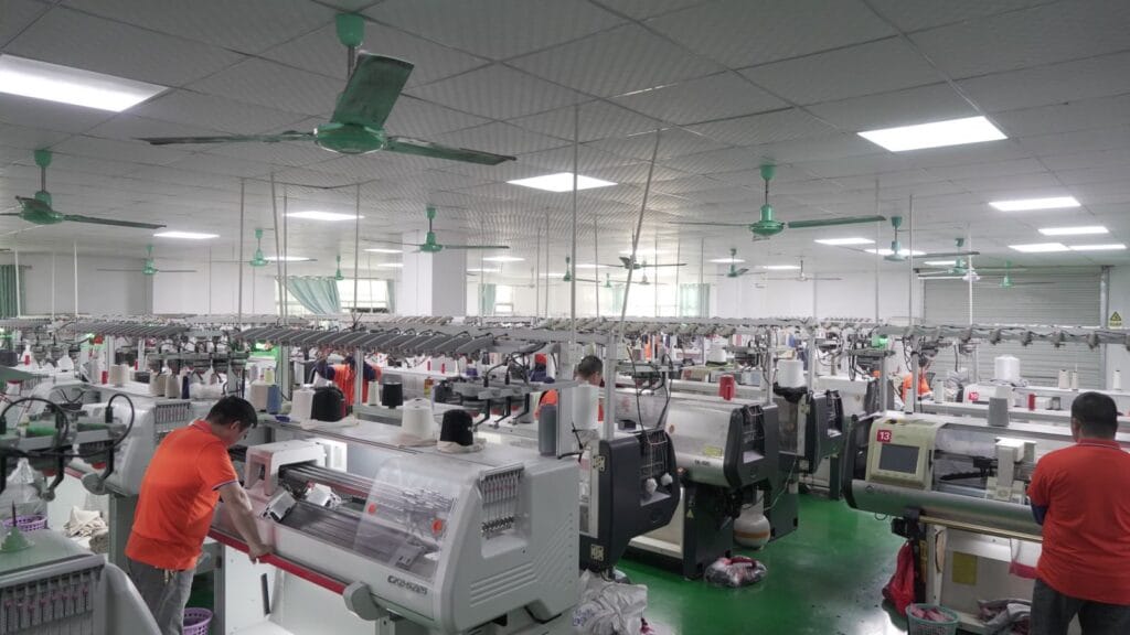 Dongguan knitwear factory production line with workers operating computerized knitting machines, custom cashmere sweater OEM manufacturing