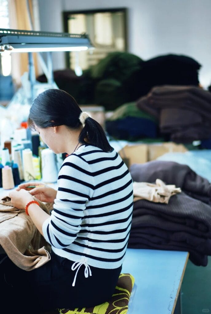 Worker doing hand finishing and thread trimming on knitwear garments in a quality control station